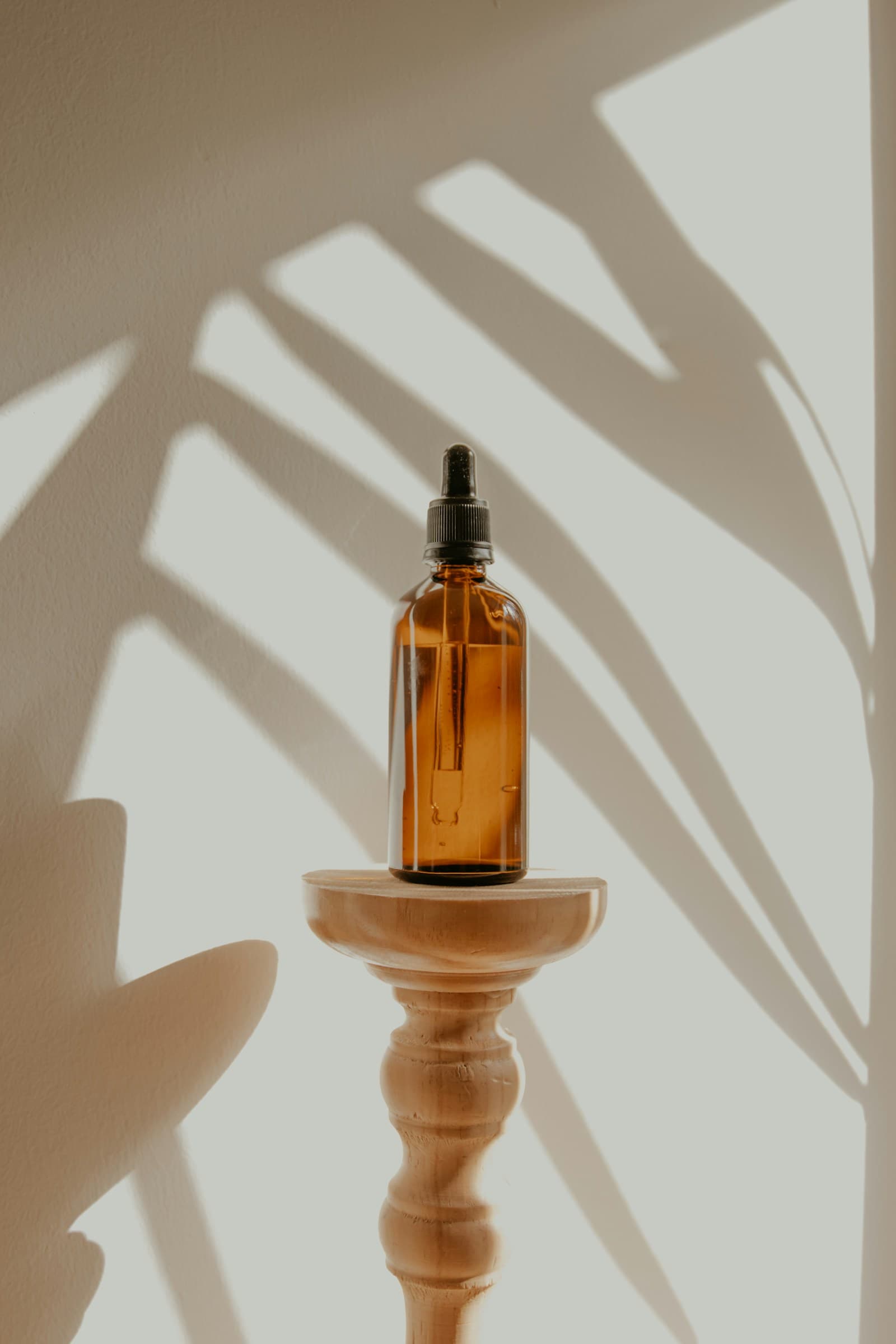 Amber dropper bottle on a wooden stand against a sunlit wall